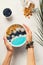 Blue smothie in bowl with granola and berries, holding hand