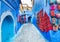 Blue street of Chefchaouen in Morocco with colorful carpets and handicrafts on walls