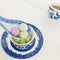 A blue-striped white porcelain spoon scoops three glutinous rice balls of different colors and flavors,with a cup of tea aside.