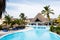 Blue sunbeds under thatch-covered sunshades stand near a swimming pool