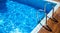 Blue swimming pool with grab ladder teak wood flooring stripes sunlight, copy space