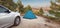 blue tent is set up on a flat area in the forest near a car. Road trips and camping in the woods