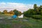 The blue tent stands on the bank of the river against the background of the forest and the blue sky with ribbon-shaped white cloud