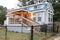 Blue tiny house in the country with warm porch lighting and a black chain fence around the yard