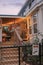 Blue tiny house in the country with warm porch lighting and a black chain fence around the yard