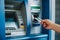 Blue top, metallic body ATM machine with hand inserting card, green CARD label, blurred background