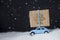 Blue toy retro car carries on a roof a Christmas gift on snow