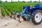 Blue tractor with a cultivator plow and the green field of the Bulgarian pepper plantation on the background. Farming, agriculture