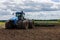 Blue tractor with double wheels pulling disc harrow with roller basket at hot sunny day