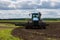 Blue tractor with double wheels pulling disc harrow with roller basket at hot sunny day