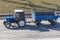 A blue tractor with an empty freight trailer rides in the city on a highway