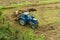 Blue tractor fertilizing a field, farmers spreading fertilizer with shovels, fertilizing fields