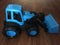 Blue tractor made of plastic on a brown wooden background. Toy blue bulldozer, side view.