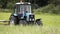 Blue tractor riding on grass field at farm near forest