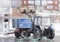 A blue tractor with a trailer clears the snow, clearing the city .Cleaning of the territory by public utilities in winter