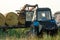 The blue tractor uses a hydraulic manipulator to stack round bales of hay in pyramids for storage and drying. Machinery works in