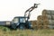 The blue tractor uses a hydraulic manipulator to stack round bales of hay in pyramids for storage and drying. Machinery works in