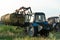 The blue tractor uses a hydraulic manipulator to stack round bales of hay in pyramids for storage and drying. Machinery works in