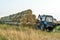 The blue tractor uses a hydraulic manipulator to stack round bales of hay in pyramids for storage and drying. Machinery works in