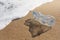 Blue transparent bottle lies on the beach near the water, casting a long shadow, nature pollution concept