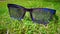 Blue transparent sun glasses or specs placed on green grass or weed surface in a garden