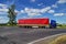 Blue truck with red sail passing a crossroads in the countryside