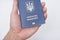 Blue Ukrainian passport in a man`s hand. White background