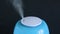 A blue ultrasonic humidifier works by releasing water vapor against a black background