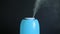 A blue ultrasonic humidifier works by releasing water vapor against a black background