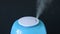 A blue ultrasonic humidifier works by releasing water vapor against a black background