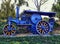 Blue vehicle with a steam engine near trees with a bright sky in the background in Trragones