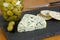 Blue veined cheese on slate with jar of stuffed olives