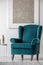 Blue velvet armchair in elegant white interior with abstract silver painting on the wall
