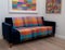 Blue velvet sofa with colourful wool blanket throw, in minimalist setting with white walls and colourful artwork.