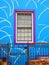 Blue wall of the house with purple window. Porch with wicket
