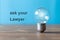 On the blue wall the words are written: ask yout lawyer. Next to the writing, an ancient light bulb with glowing light stands free