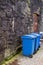 Blue waste bins on wheels in old town by a stone wall,