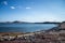 Blue water filled lake dam with rocky foreshore and small hills in background against blue sky