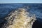 Blue water of lake with waves and white foam from a boat, clear sky on the horizon