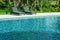 Blue water in swimming pool with black weave daybed and green trees in background.