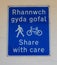 Blue and white bilingual sign encouraging cyclists and pedestrians to share the pavement Llandudno North Wales May 2019