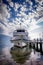 Blue & white boat moored at lakeside jetty with dramatic sky and cloud reflections in the water