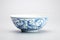 A blue and white bowl sitting on top of a table. Imaginary oriental pottery.