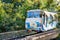 A blue-and-white cable funicular rises on rails along the slope among the green foliage of the trees