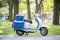 blue and white delivery scooter with side bags near a park