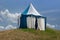 Blue and white medieval tent standing on the hill top with blue sky and white clouds