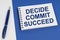On a blue-white surface lies a pen and a notebook with the inscription - Decide Commit Succeed