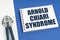 On a blue-white surface lies a stethoscope and a notepad with the inscription - Arnold Chiari Syndrome