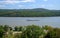 Blue and white tug boat was seen pushing a long barge down the Hudson River. There are small green tree covered hills in the.