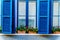Blue windows with Shutters and red geraniums on the window sill of a house